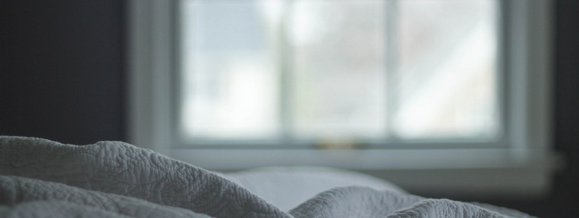 The top of a blanket laying on a bed with a window in the background.